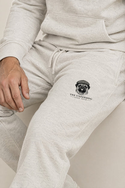 Close-up of The Underdog Golf Club pug crest on the left thigh of the Oat Gray sweatpants. Color: Oat Gray