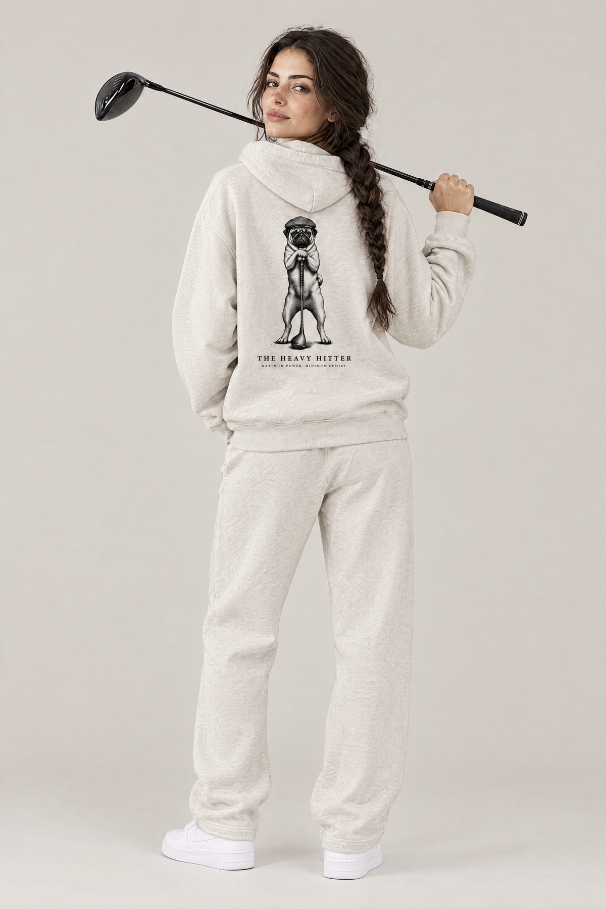 Woman with a driver over her shoulder, back view of The Heavy Hitter pug golf hoodie in Oat Gray with the large back print. Color: Oat Gray