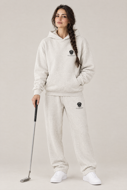 Woman holding a putter in The Heavy Hitter pug golf hoodie and matching Underdog Golf Club sweatpants in Oat Gray, front view. Color: Oat Gray