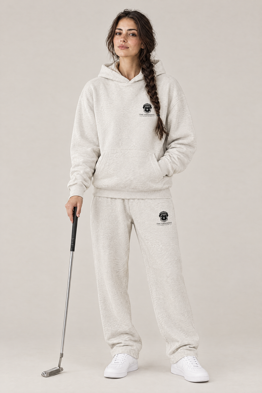 Woman holding a putter in The Heavy Hitter pug golf hoodie and matching Underdog Golf Club sweatpants in Oat Gray, front view. Color: Oat Gray
