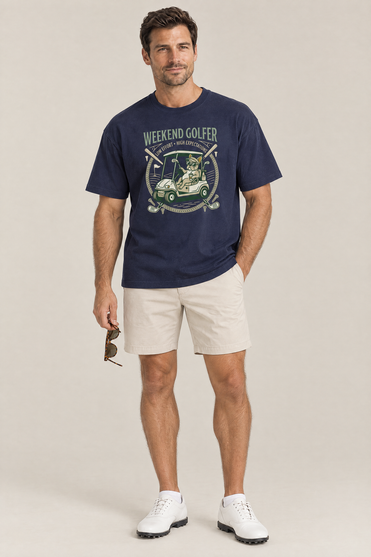 Man wearing the Weekend Golfer French Bulldog Golf Tee in navy with stone golf shorts holding sunglasses. Color: Navy