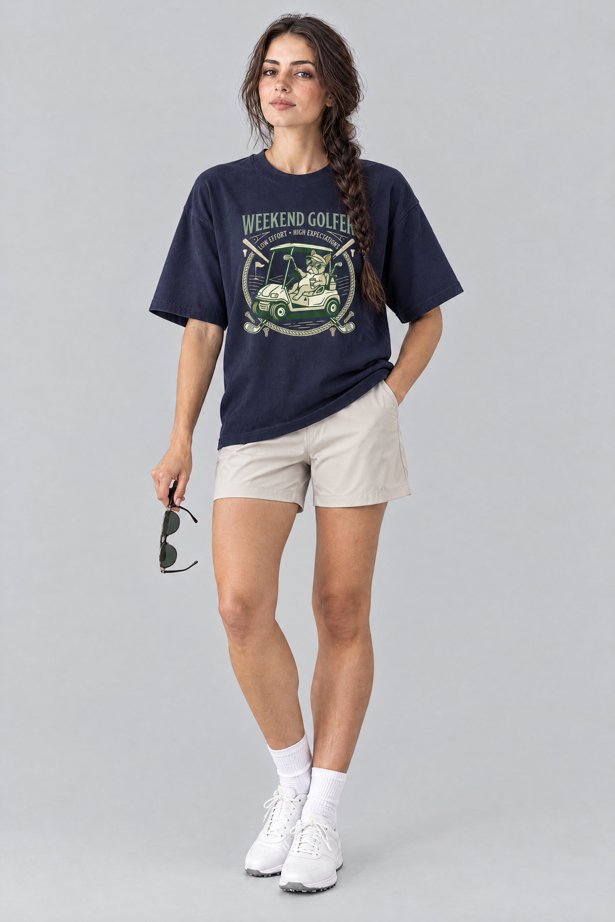 Woman wearing the Weekend Golfer French Bulldog Golf Tee in navy with stone golf shorts, holding sunglasses. Color: Navy