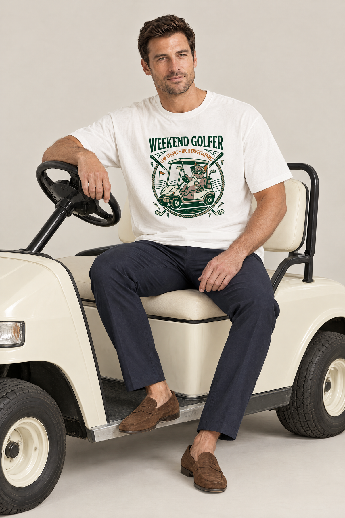 Man sitting on a golf cart in the white Weekend Golfer French Bulldog Golf Tee. Color: White