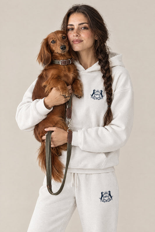 Woman in the white Club Crest hoodie and sweatpants holding a long-haired dachshund wearing the Cloud 7 Tivoli Olive collar