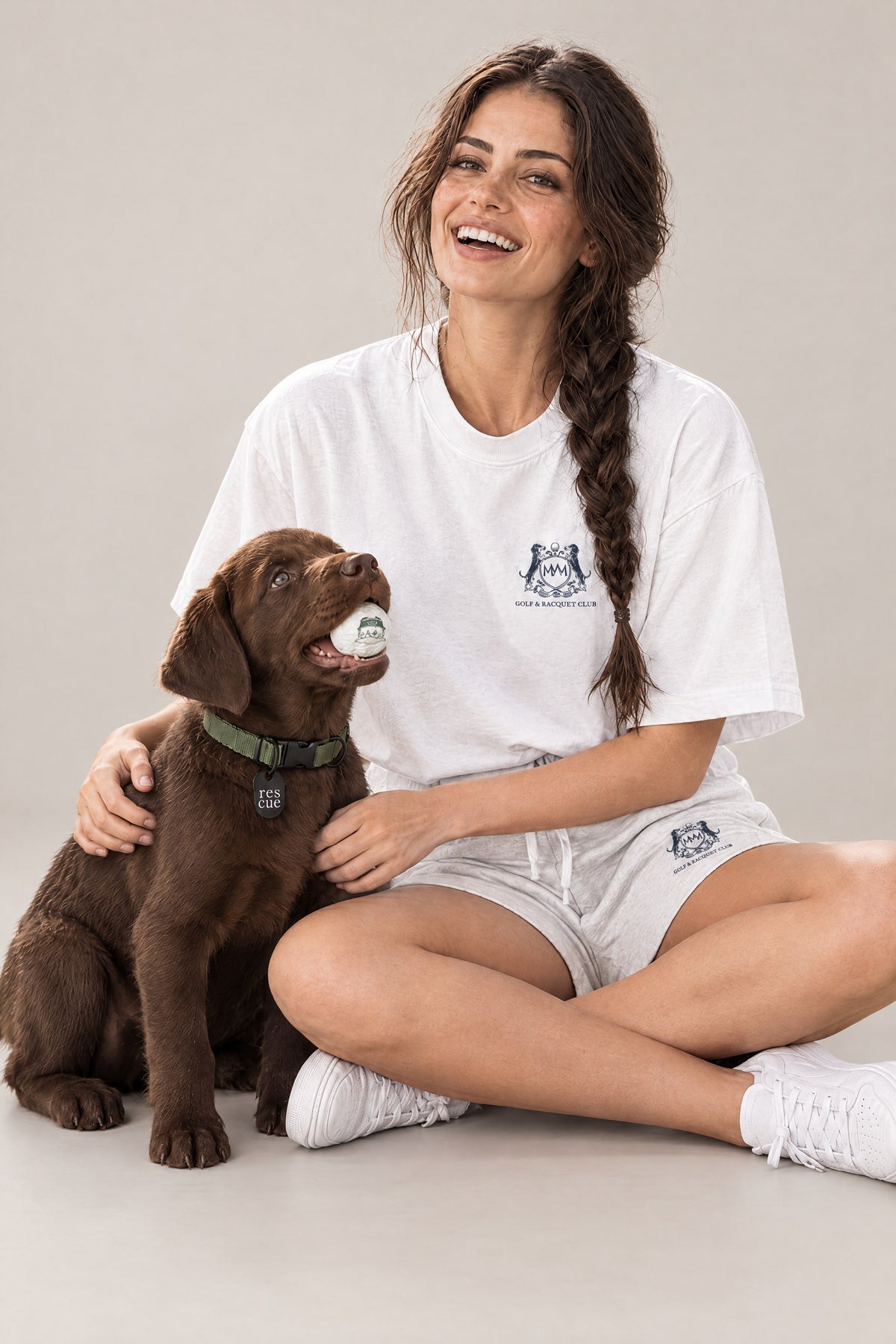 Woman in the white Club Crest tee sitting with a chocolate Labrador puppy wearing the green Cloud 7 RESC7UE collar