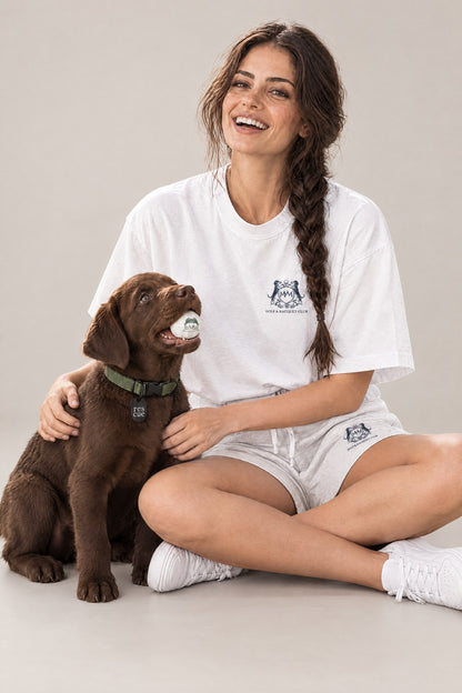 Woman in the white Club Crest tee sitting with a chocolate Labrador puppy wearing the green Cloud 7 RESC7UE collar