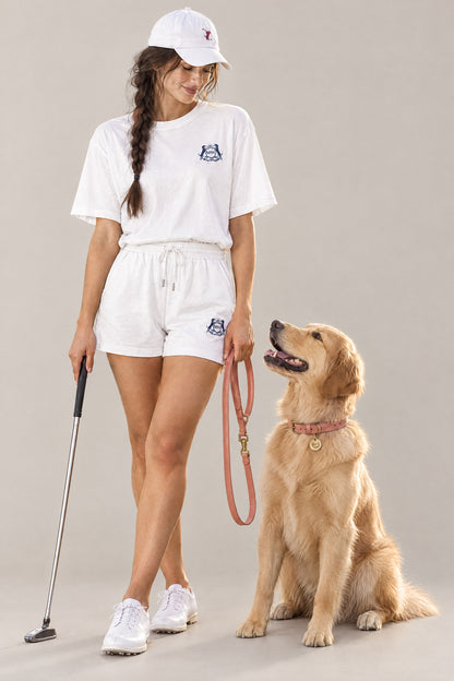 Woman in the white Club Crest tee holding a putter next to a Golden Retriever wearing the peach Cloud 7 Tiergarten collar and leash