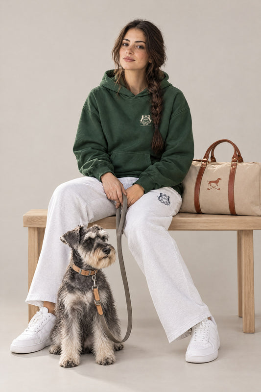 Woman in the blackish green Club Crest hoodie seated with a Miniature Schnauzer on the greige Cloud 7 Tivoli leash