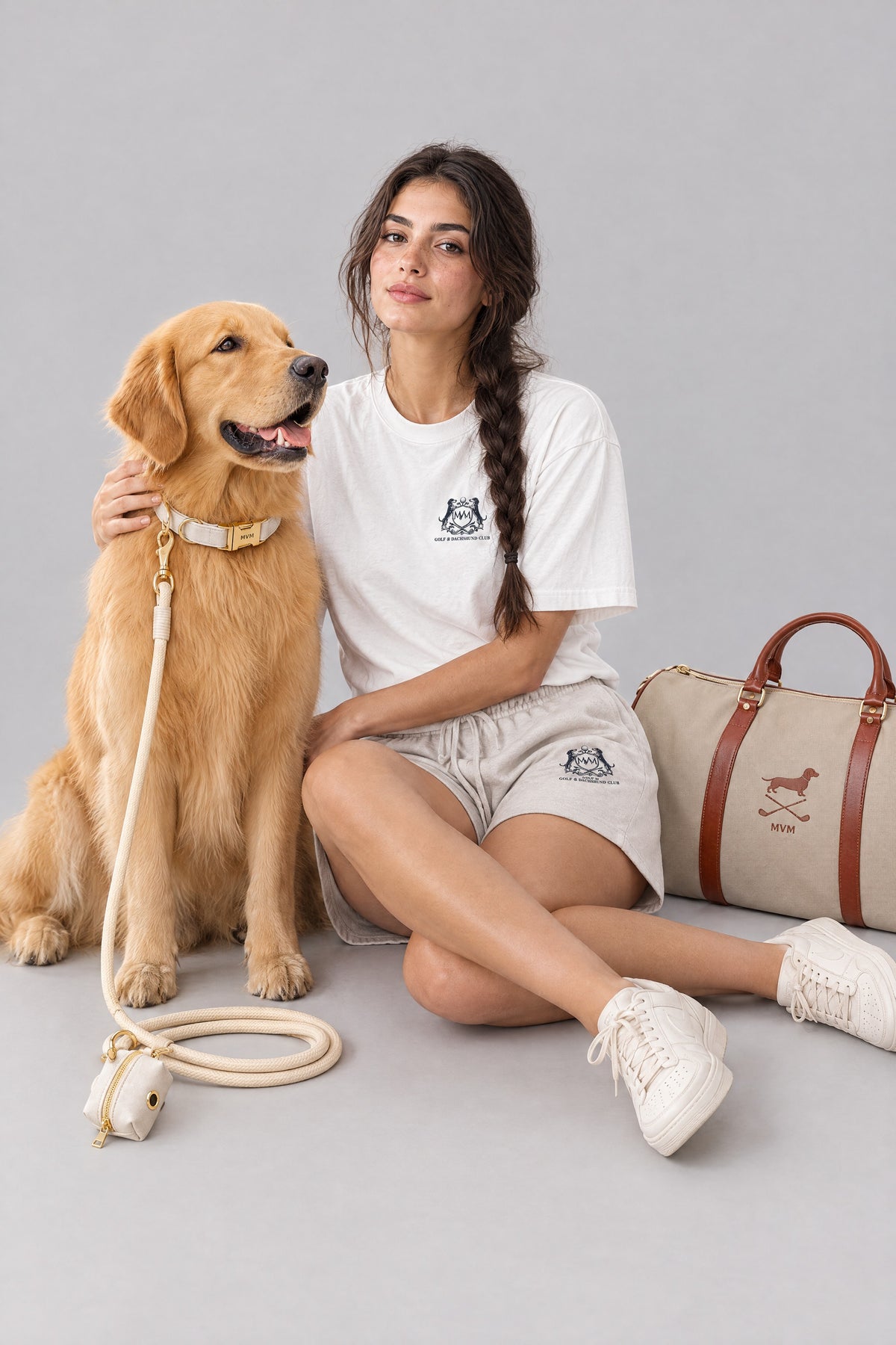 Woman in the white Club Crest tee and oat Club Crest shorts sitting with a Golden Retriever wearing the warm beige MVM Evergreen set