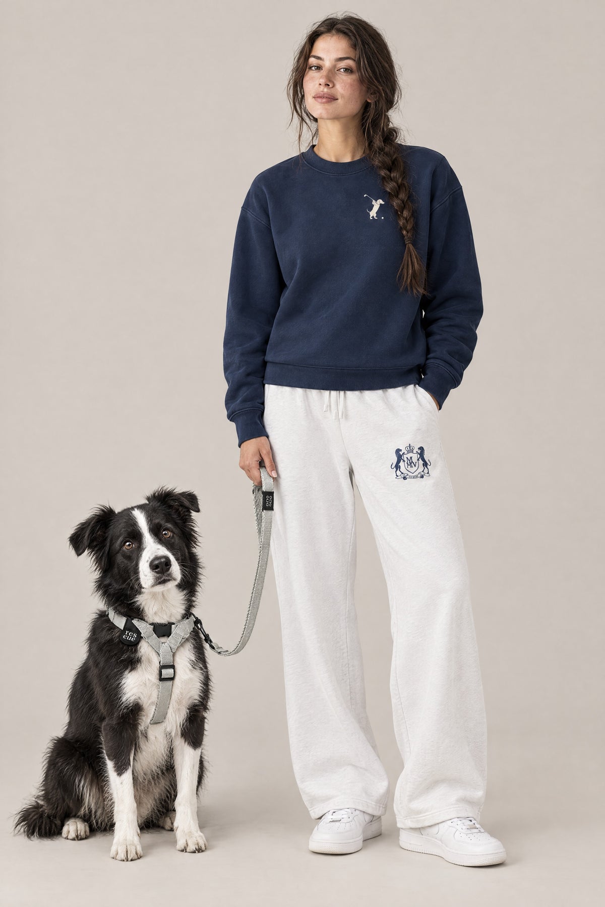 Woman in the navy Swing dachshund golf sweatshirt and white Club Crest sweatpants with a border collie mix in the silver Cloud 7 RESC7UE harness and leash